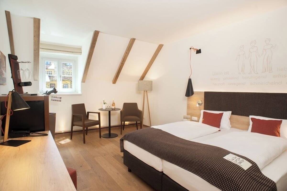 Una habitación de hotel con cama, escritorio, sillas, lámpara y ventana.