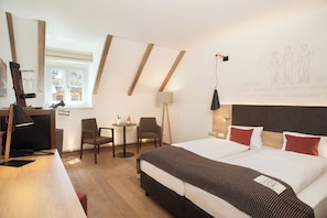 A hotel room with a bed, desk, chairs, a lamp, and a window.