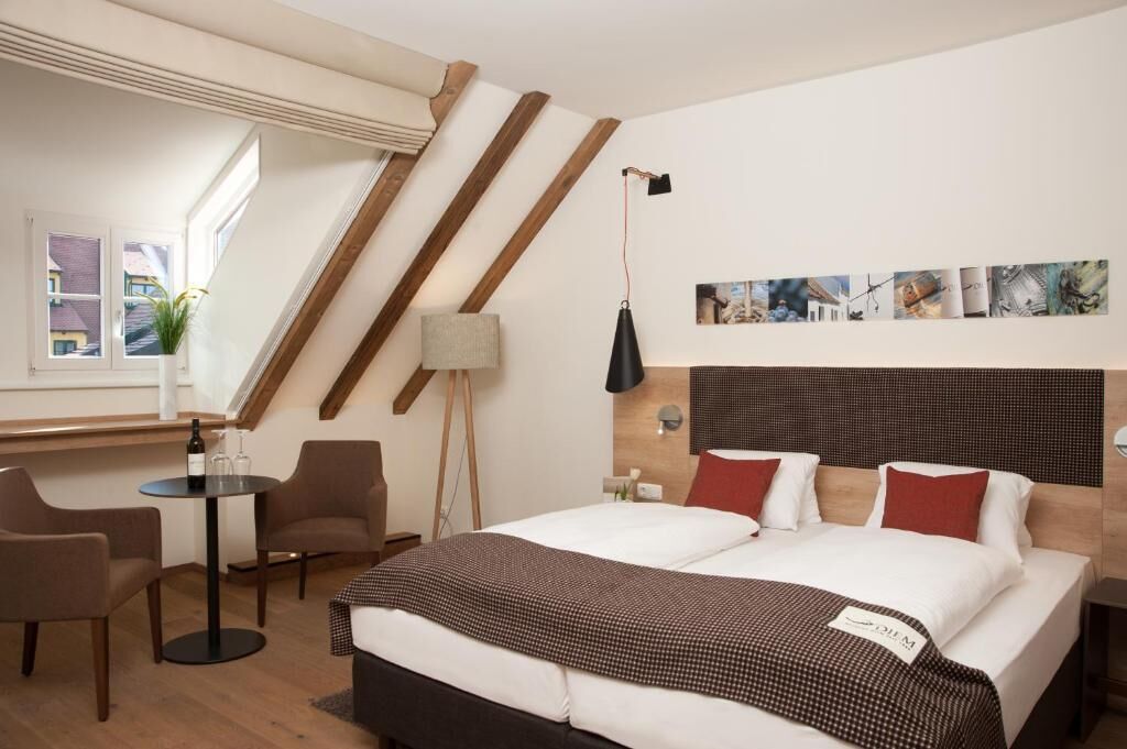 Habitación de hotel con cama, dos sillas, una mesa, una lámpara y una ventana con vistas.