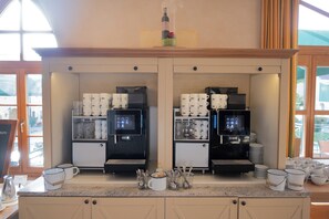 Una estación de café con dos máquinas de espresso, tazas y una cafetera.