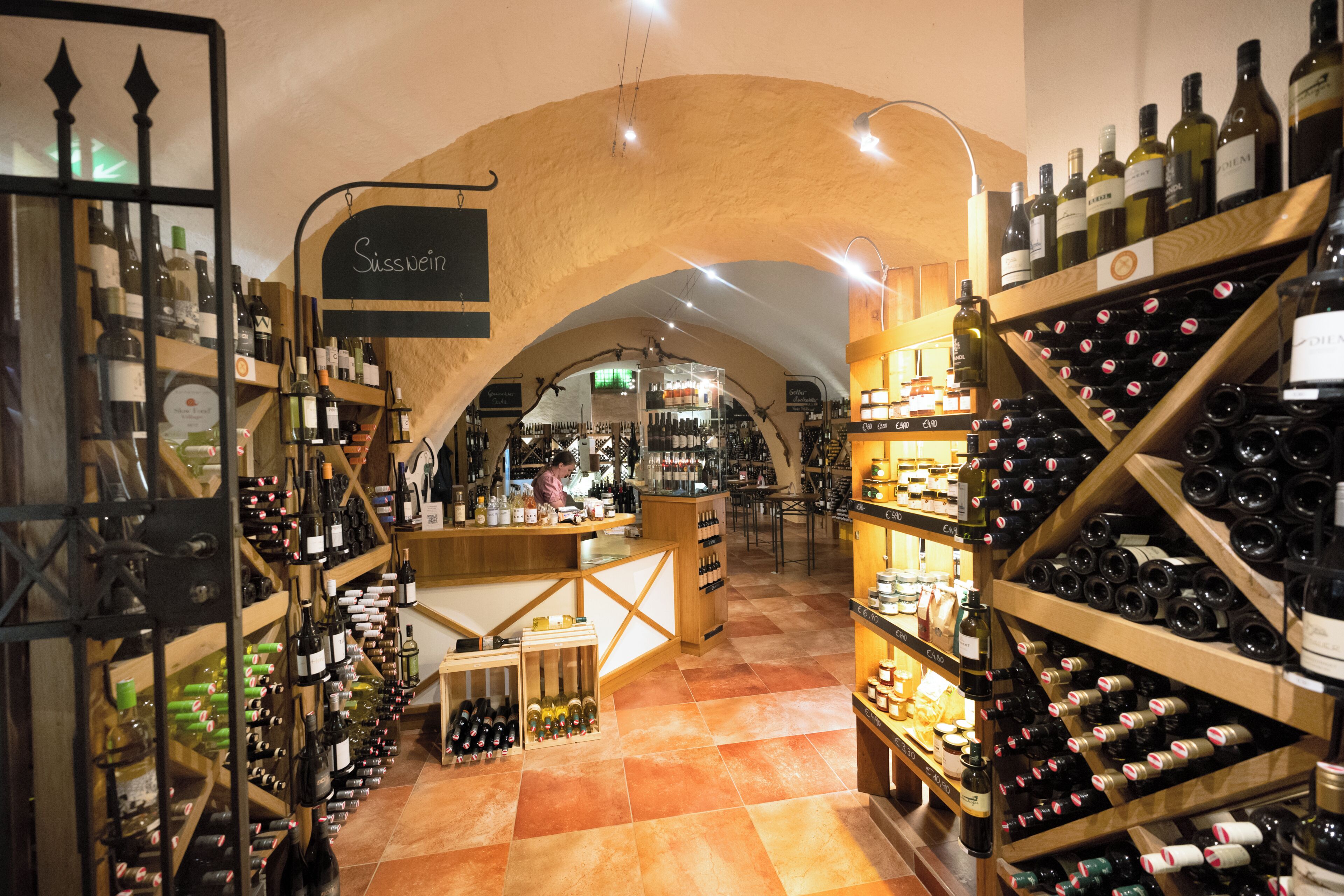 A wine shop with shelves of wine bottles, a counter, and a vaulted ceiling.