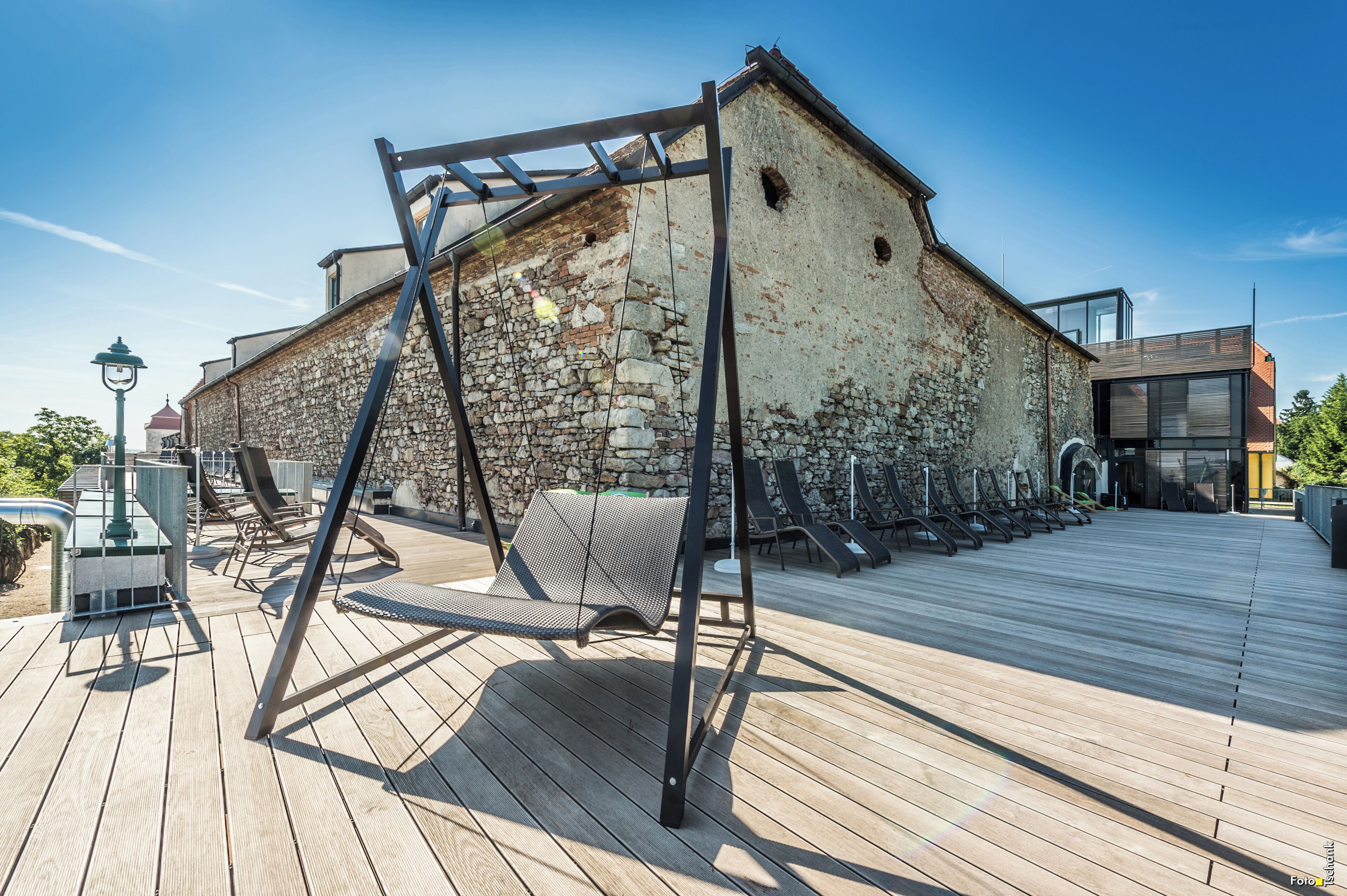 A wooden deck with a swing set, a stone building, and a modern structure with glass windows.