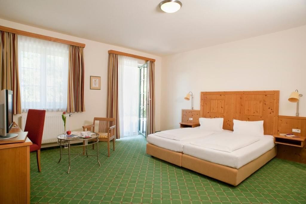 A hotel room with a large bed, a desk with a chair, a small table, and a television.