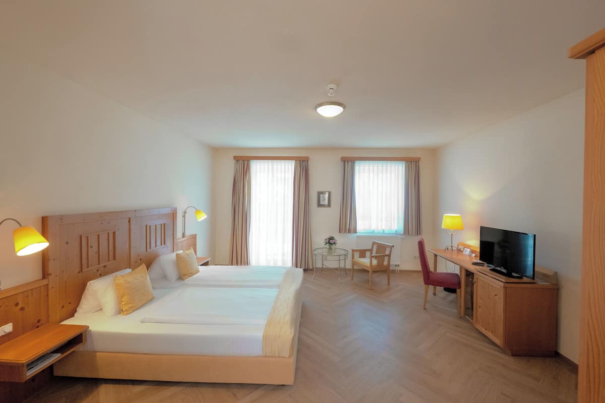 Habitación de hotel con una cama grande, un escritorio con televisor, una silla y una mesita con lámpara.