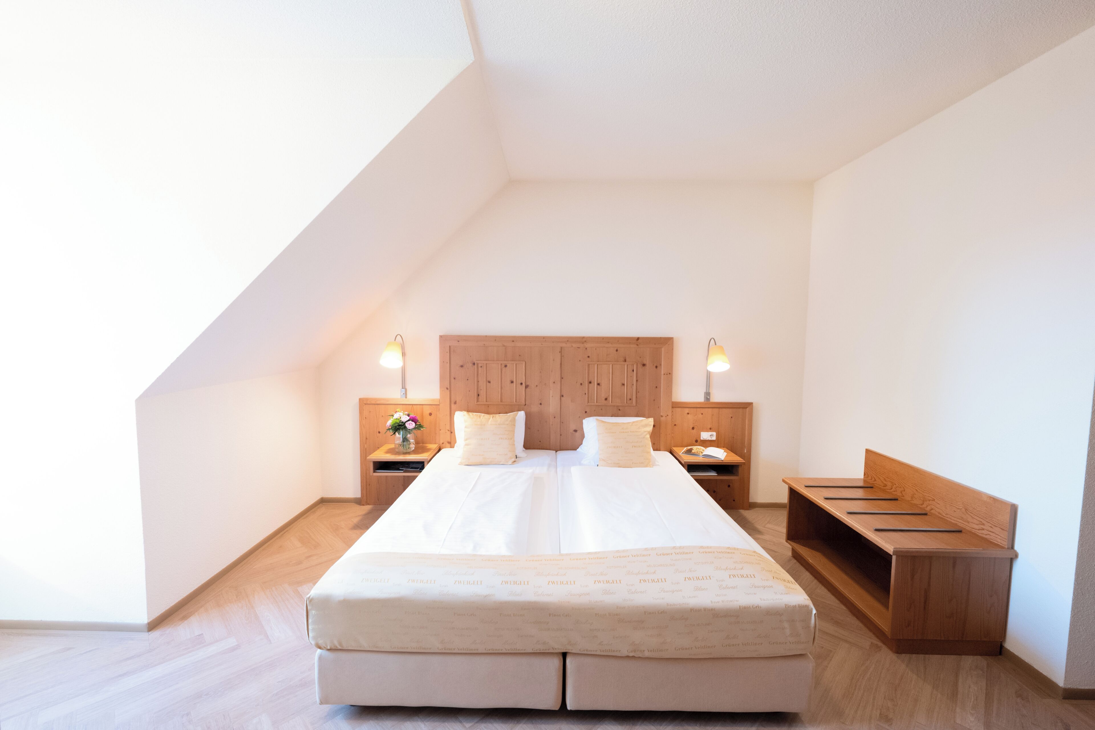 Un dormitorio con una cama grande, cabecera de madera, mesitas de noche con lámparas y un banco.
