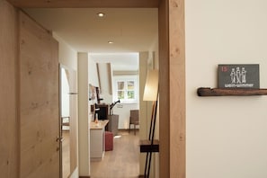 A hallway leading to a room with a wooden door, a lamp, and a framed artwork on the wall.