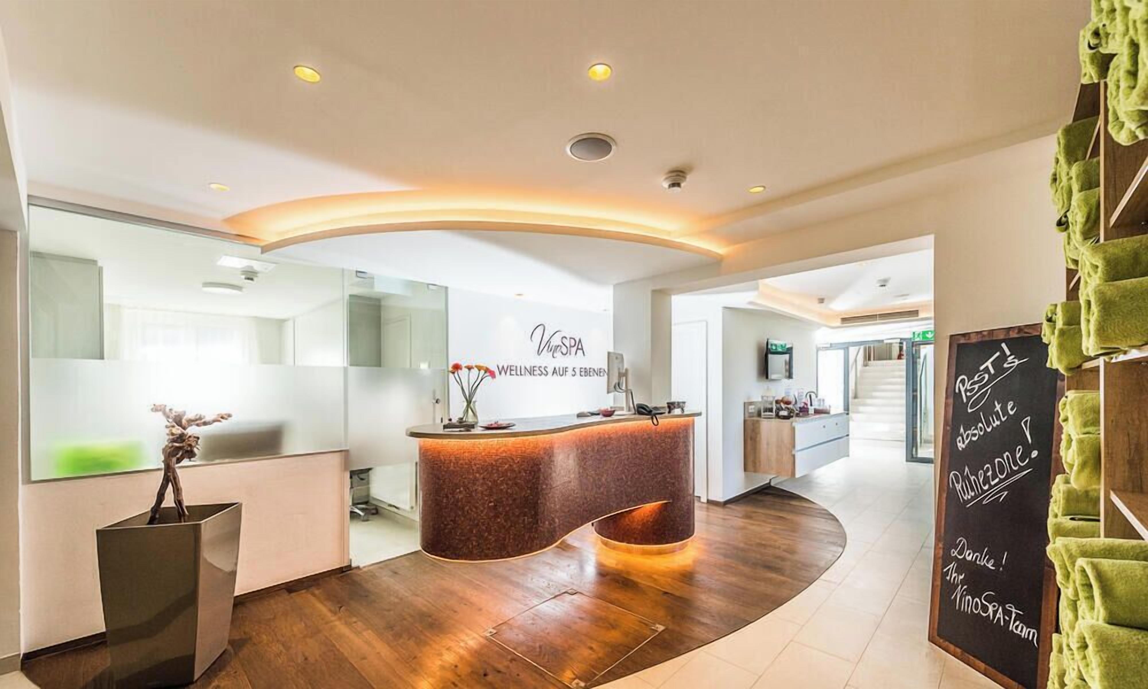 A modern spa reception area with a curved counter, a reception desk, and a chalkboard sign.