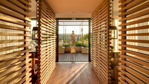 A corridor with wooden slats on both sides, leading to a balcony with a statue and a view of greenery.