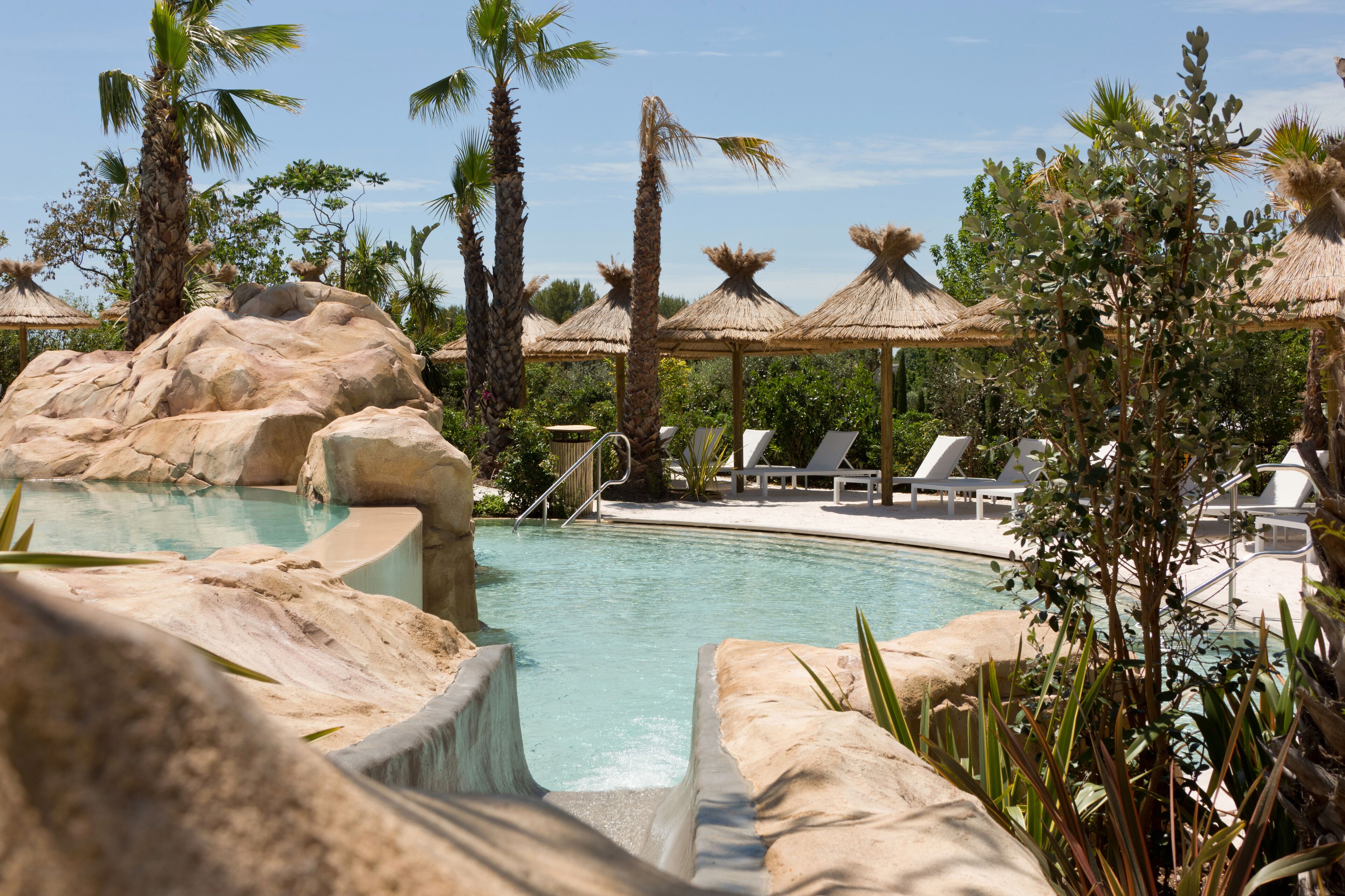 A pool area with rock formations, lounge chairs, and palm trees.