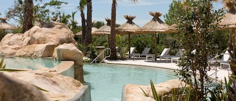 A pool area with rock formations, lounge chairs, and palm trees.