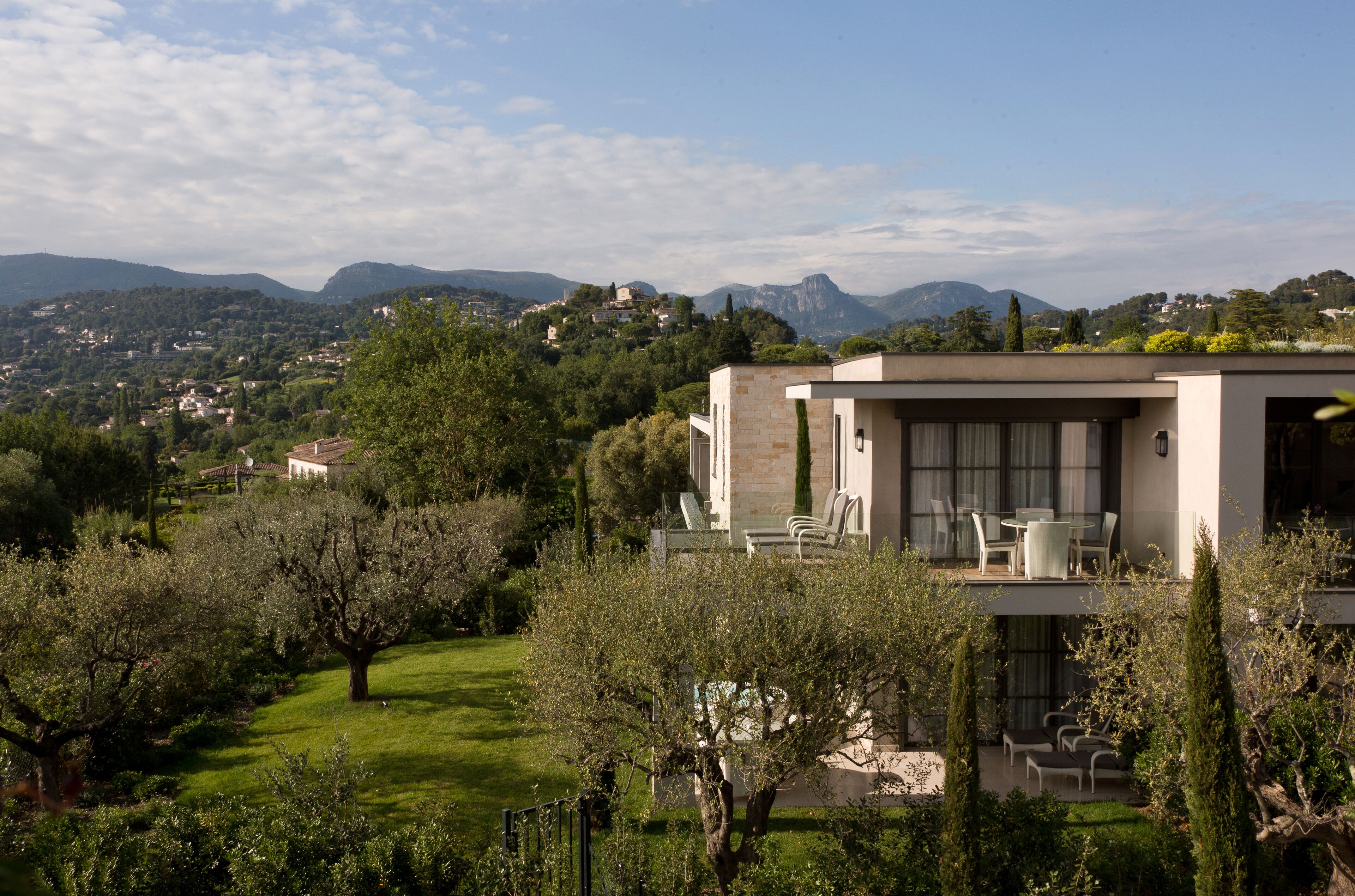 A modern house with a balcony overlooking a lush garden and distant mountains.