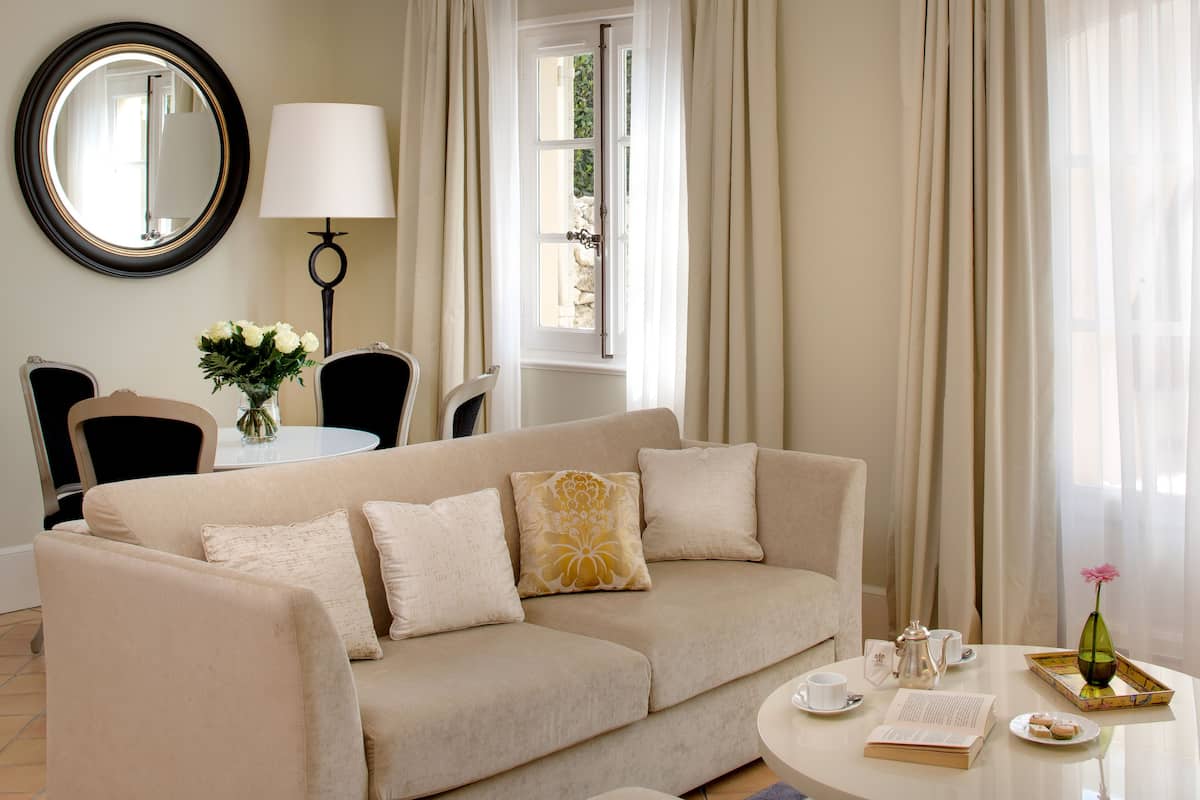 A modern living room with a beige sofa, a round mirror, a table with a lamp, and a window with curtains.