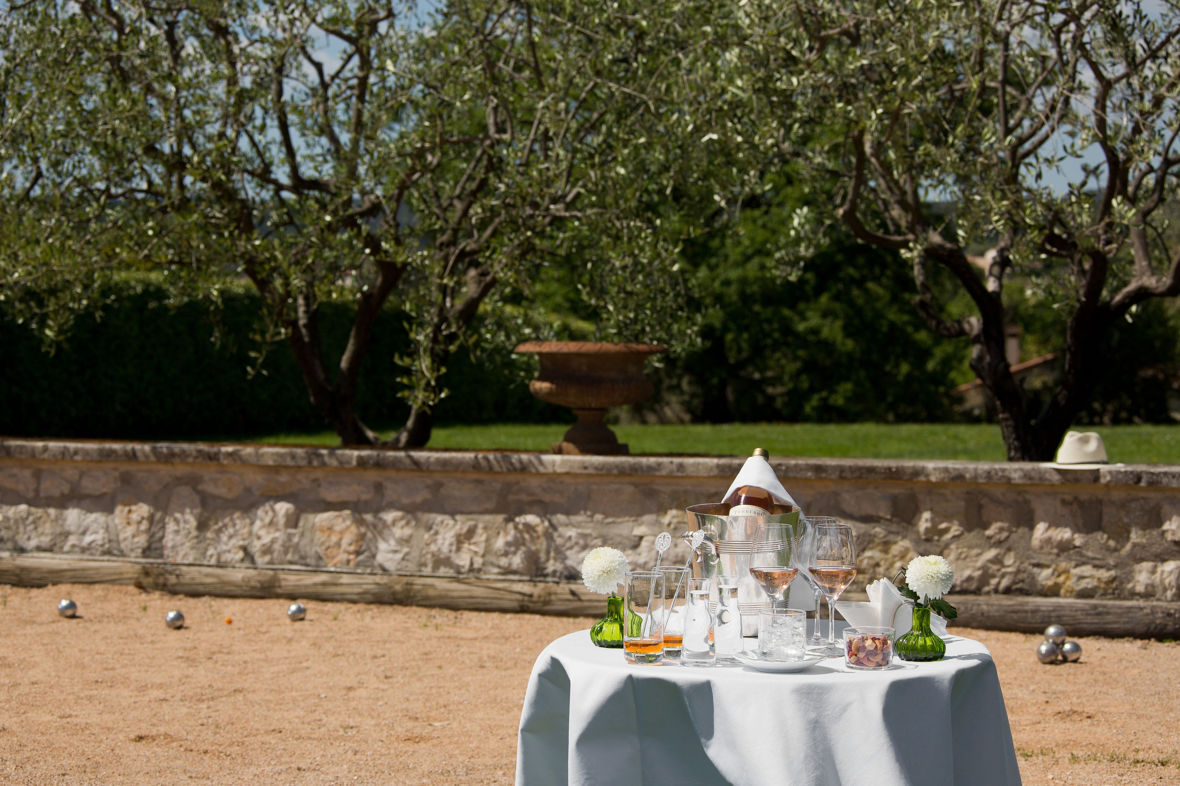 An outdoor table set with glassware and flowers, surrounded by a stone wall and trees.