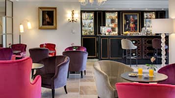 Eine Bar mit einer Theke, Regalen voller Flaschen und einem Gemälde. Mehrere Stühle und ein Tisch mit Speisen und Getränken sind ebenfalls vorhanden.