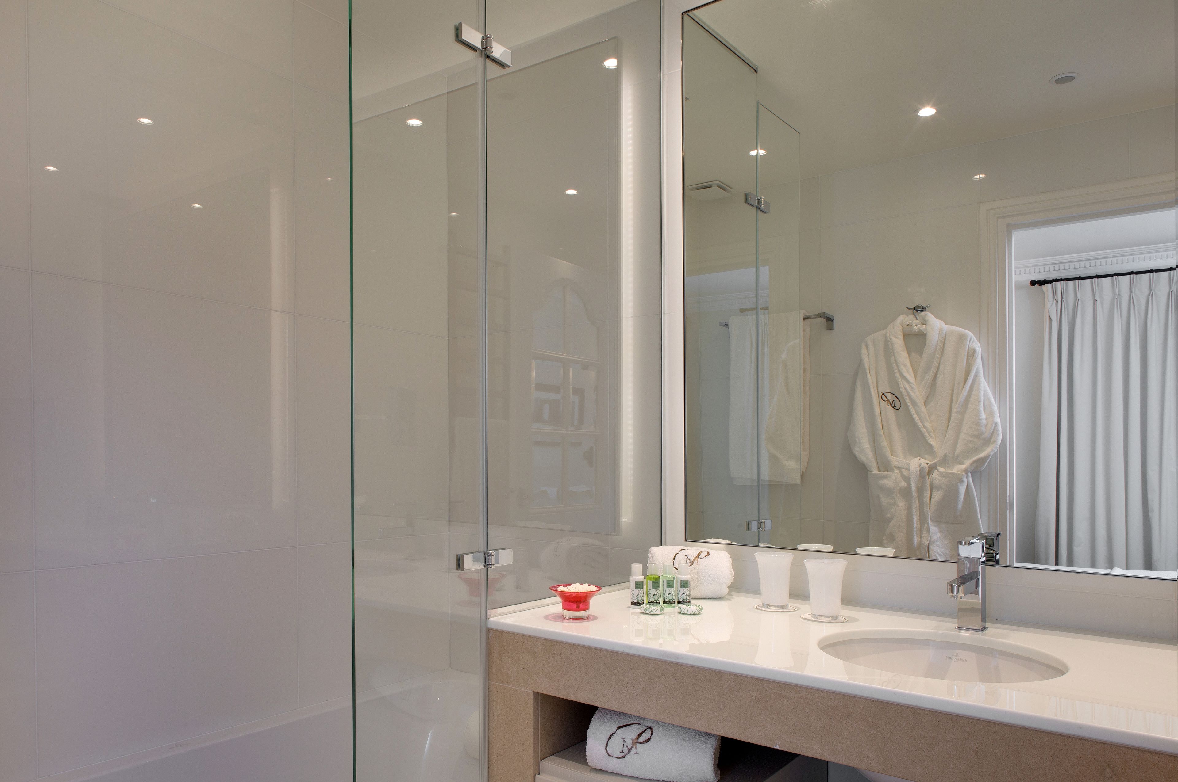 A modern bathroom with a glass shower enclosure, a large mirror, and a vanity with toiletries.