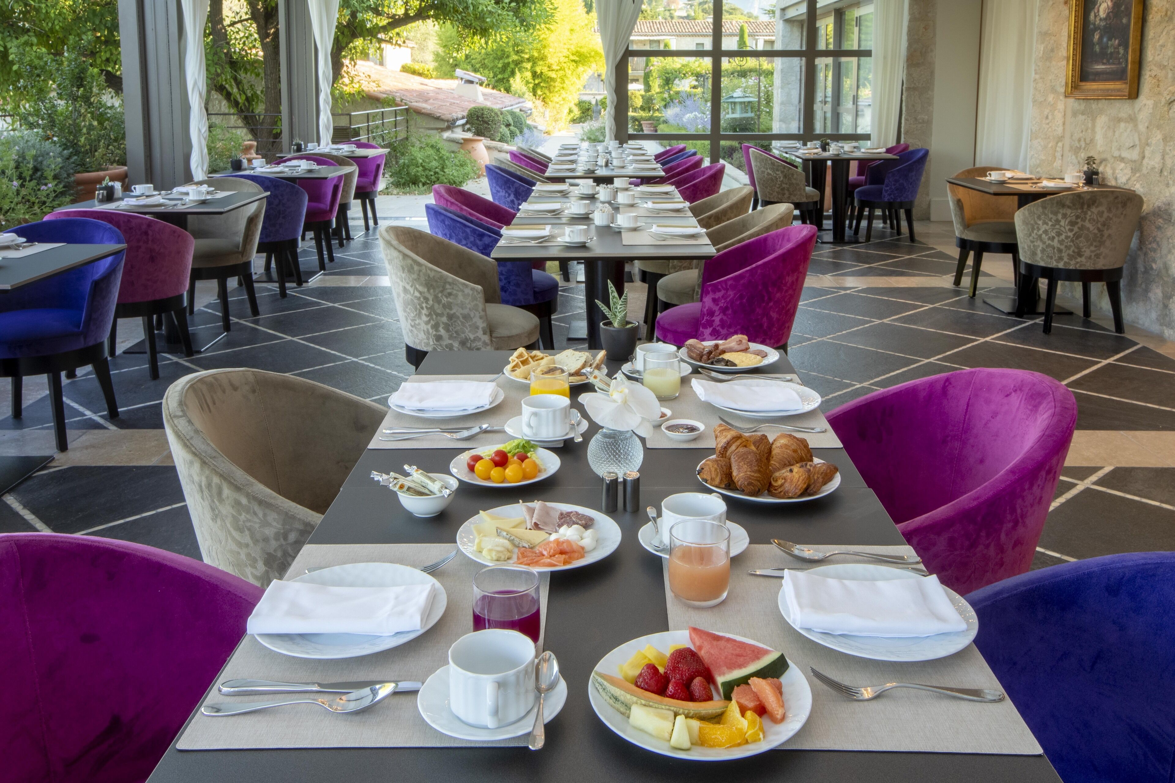 A restaurant with a long dining table set for breakfast, surrounded by purple and beige chairs.