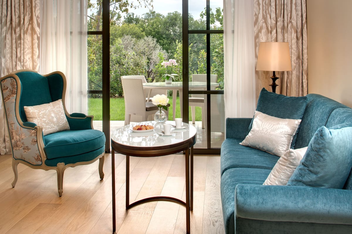 A room with a teal armchair, a blue sofa, and a glass table with a vase and a plate of food.