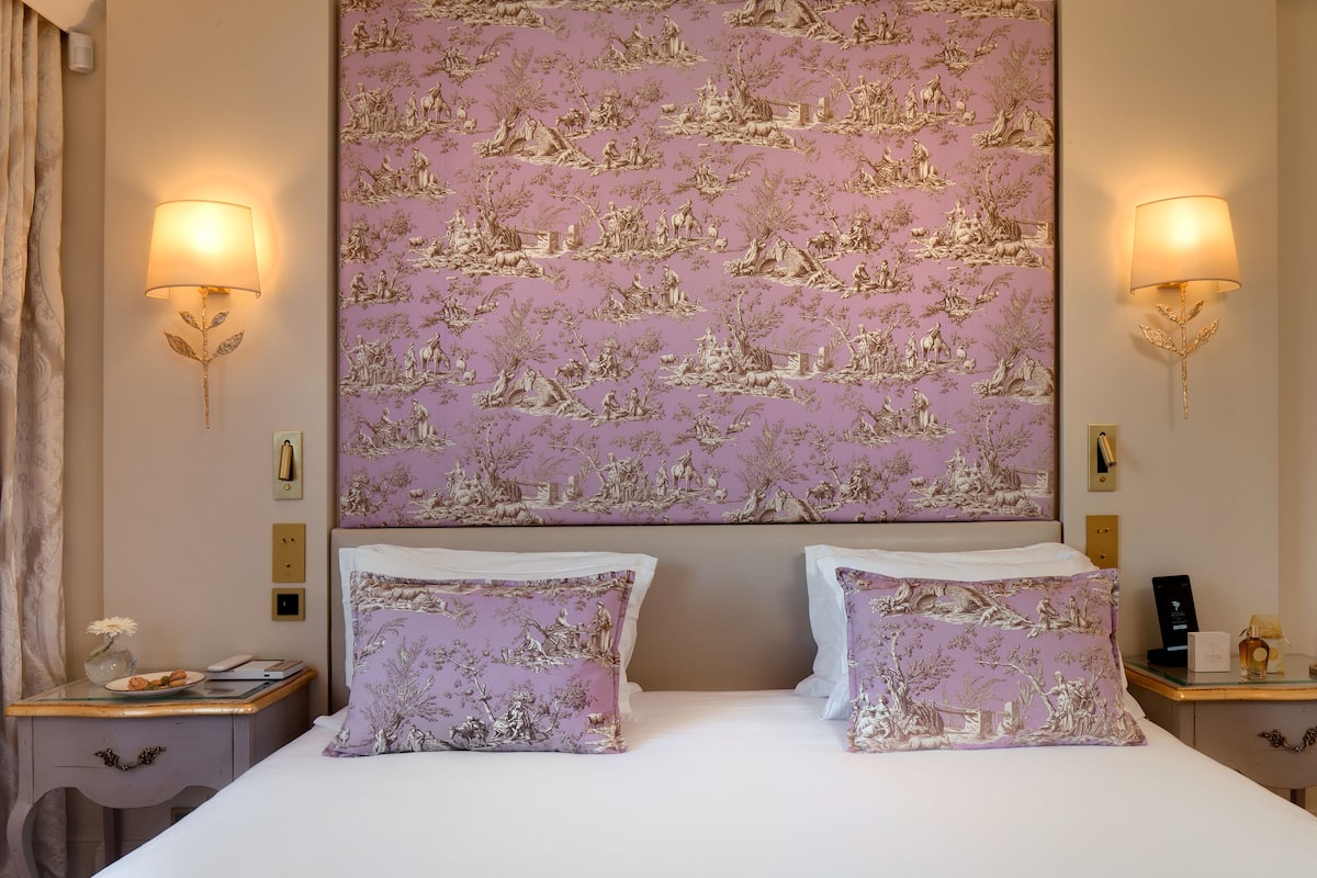 A hotel room with a large bed, two nightstands, a wall-mounted lamp, and a decorative headboard.