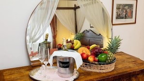 A room with a bed, a mirror reflecting a bed, a fruit basket, a bottle, and a tray with glasses.