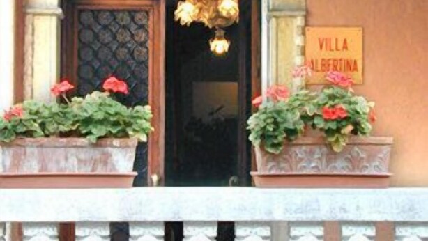 A building entrance with a sign reading "Villa Albertina," a decorative archway, and two flower planters on the porch.