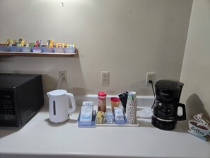 Una encimera de cocina con una cafetera, un hervidor y varios tipos de cápsulas de café y utensilios.