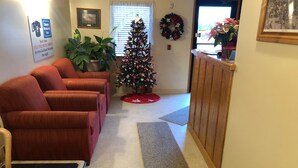 Un hall d’hôtel décoré d’un sapin de Noël, avec des canapés rouges, un comptoir d’accueil en bois et une enseigne indiquant « Simple Rewards Inn ».