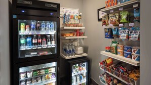 A vending machine with various drinks and snacks, a refrigerated display case with dairy products, and shelves stocked with packaged goods. - Spark by Hilton Houston West Clay Road (Houston)
