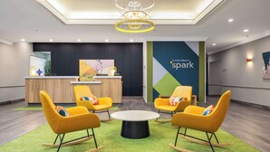 A modern reception area with a wooden desk, yellow rocking chairs, and a green carpet. - Spark by Hilton Houston West Clay Road (Houston)
