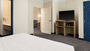 A hotel room with a bed, a television on a wooden stand, a door, and a small table with a lamp. - Spark by Hilton Houston West Clay Road (Houston)