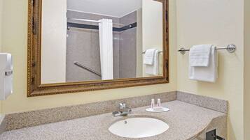 A bathroom with a granite countertop sink, a large mirror, and a shower visible in the background.