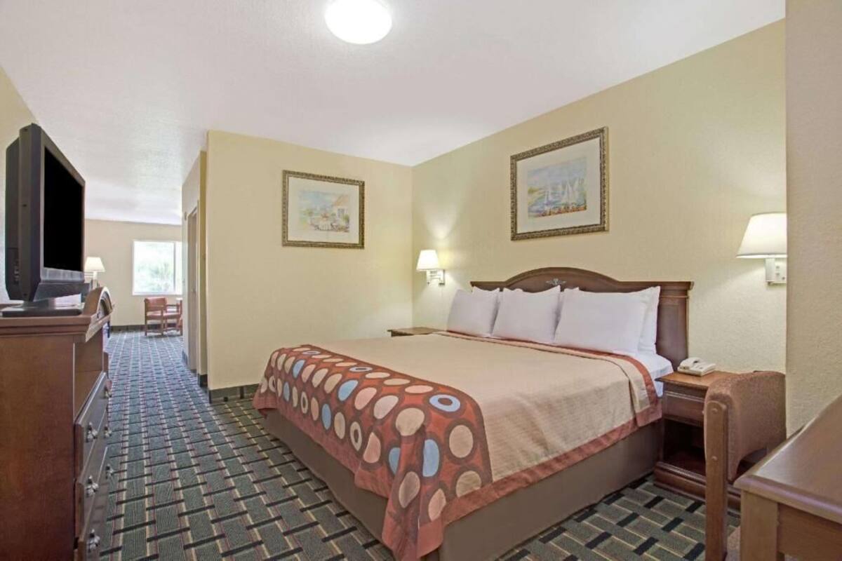 A hotel room with a bed, a desk, a television, two framed pictures on the wall, and a patterned carpet.