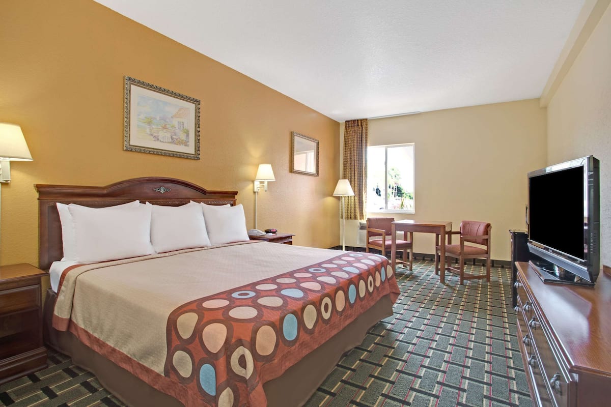 Une chambre d’hôtel avec un grand lit, un bureau, une chaise, une télévision et une fenêtre avec des rideaux.