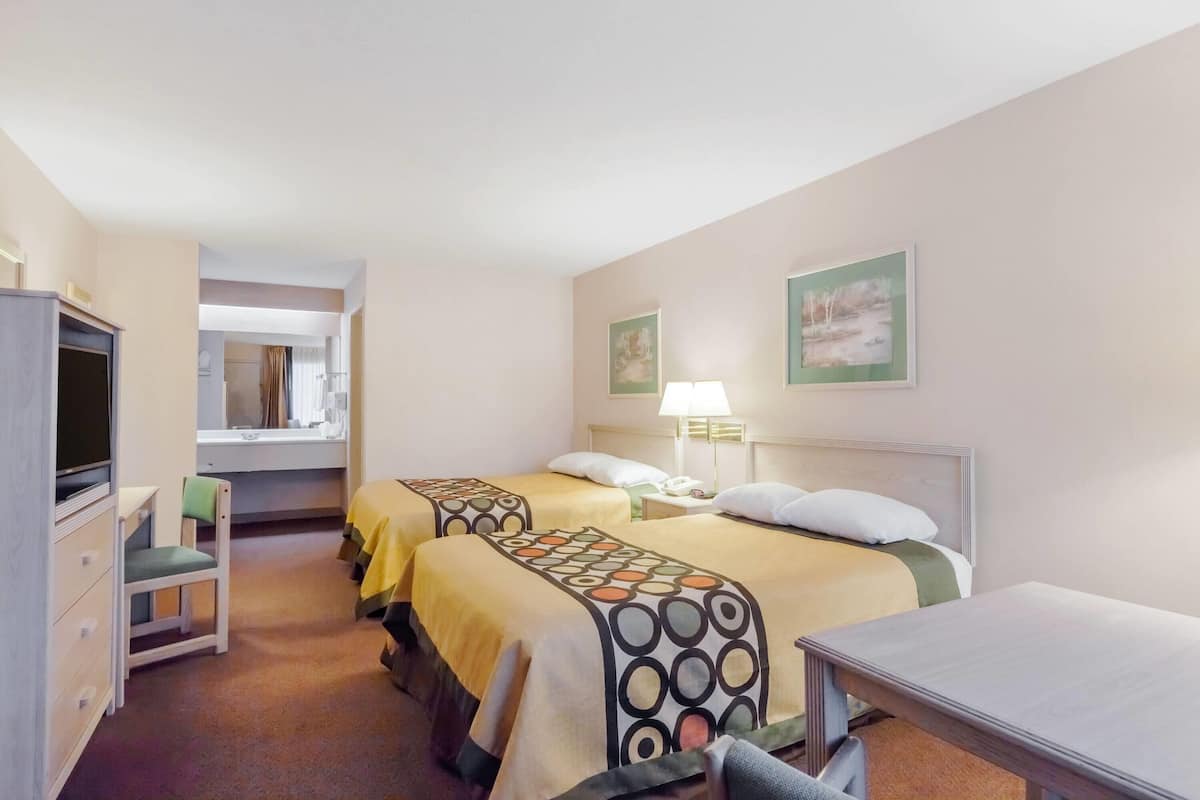 Une chambre d’hôtel avec deux lits, un bureau, une chaise et un téléviseur.