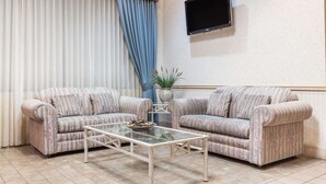 Ein Wohnzimmer mit zwei gestreiften Sofas, einem Glastisch, einem Flachbildfernseher und einer Topfpflanze.