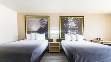 Ett hotellrum med två separata sängar, ett litet bord mellan dem och ett mindre bord med en lampa.