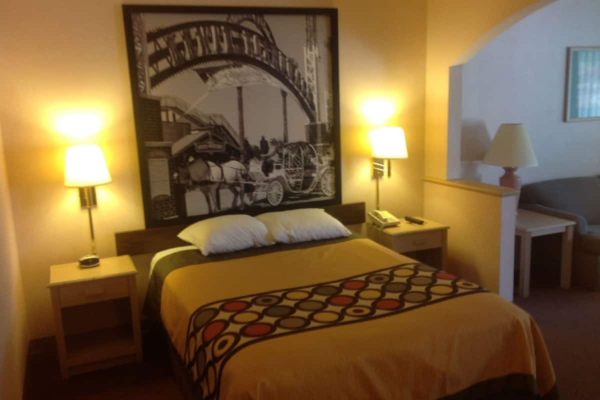 Une chambre d’hôtel comprenant un lit, deux tables de chevet, une petite table, une lampe, une chaise et une œuvre d’art accrochée au mur.