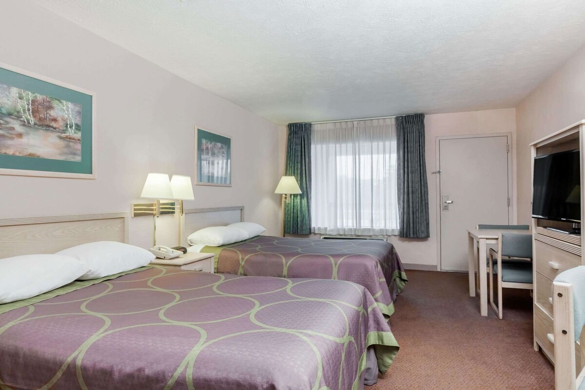 A hotel room with two beds, a desk, a television, and a painting on the wall.