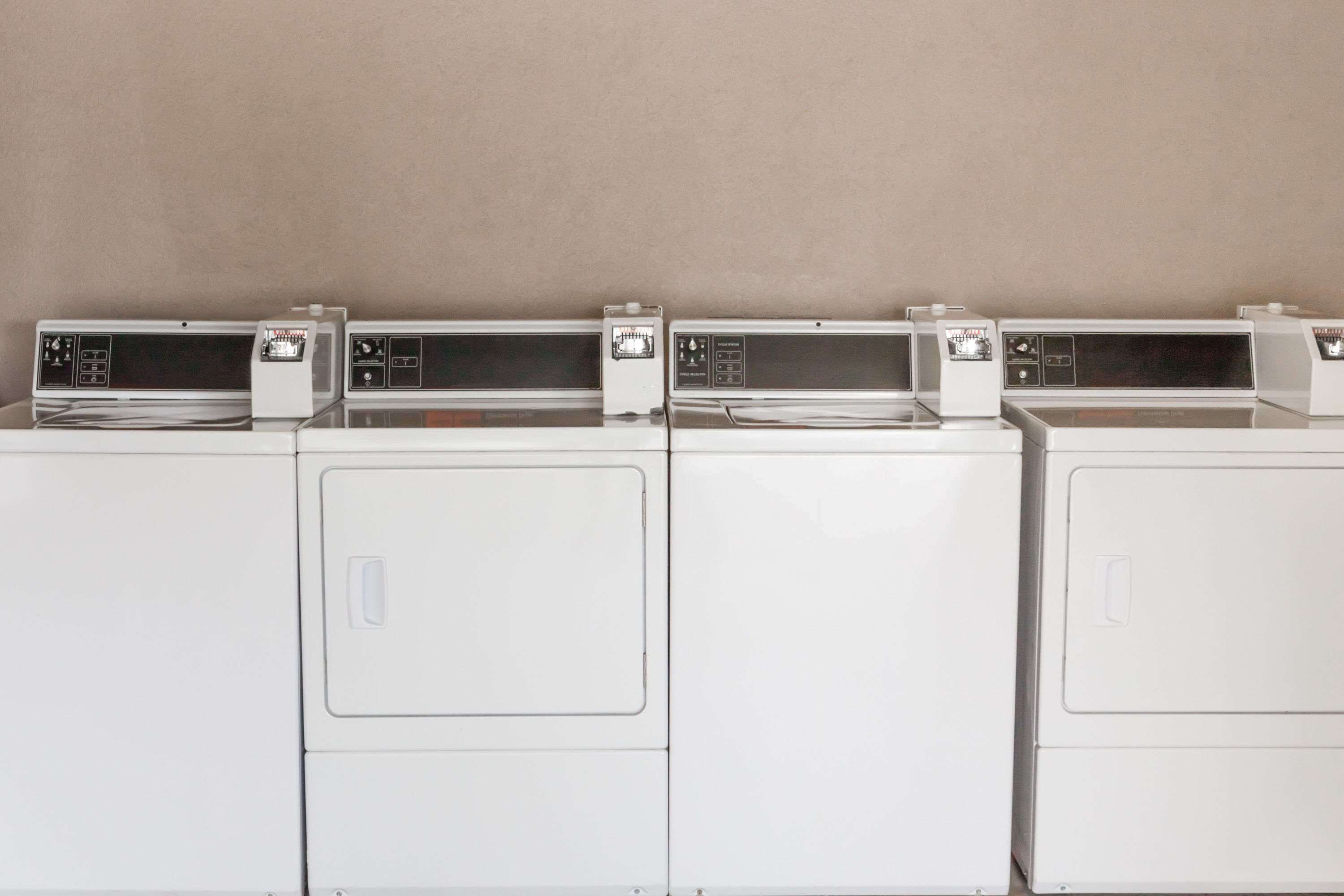 A row of white stacked washer-dryer units against a plain wall.