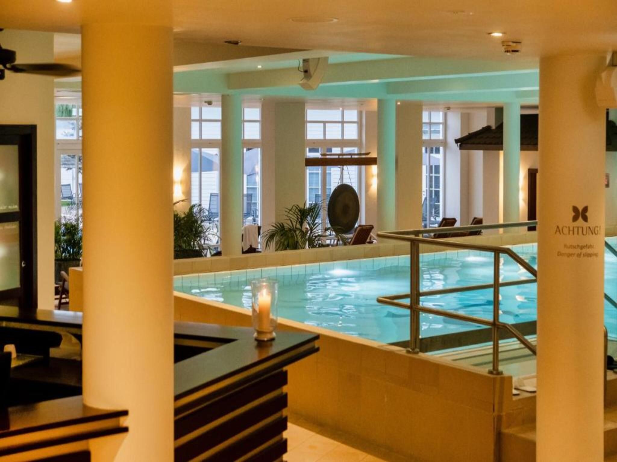 A pool area with a glass barrier, a candle on a table, and a sign reading 'Achtung! Danger of slipping.'
