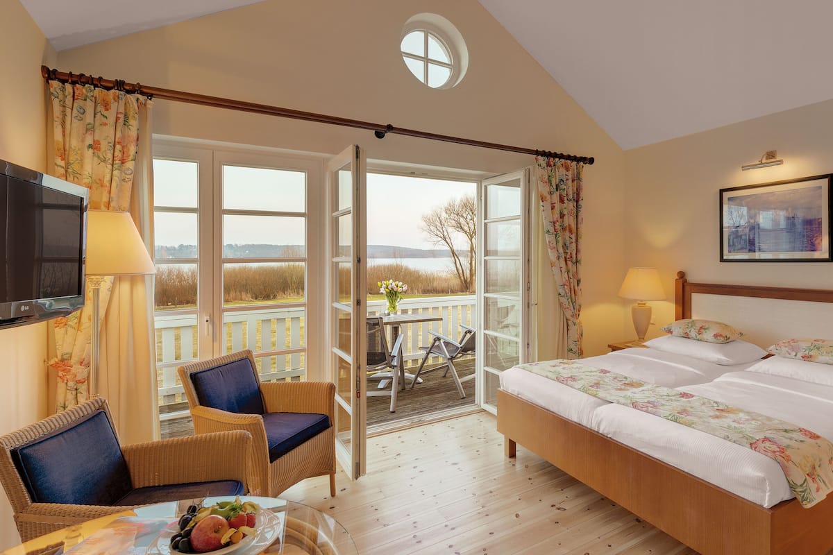 A bedroom with a large bed, a TV, a dining table with fruit, and a balcony with a view of the landscape.