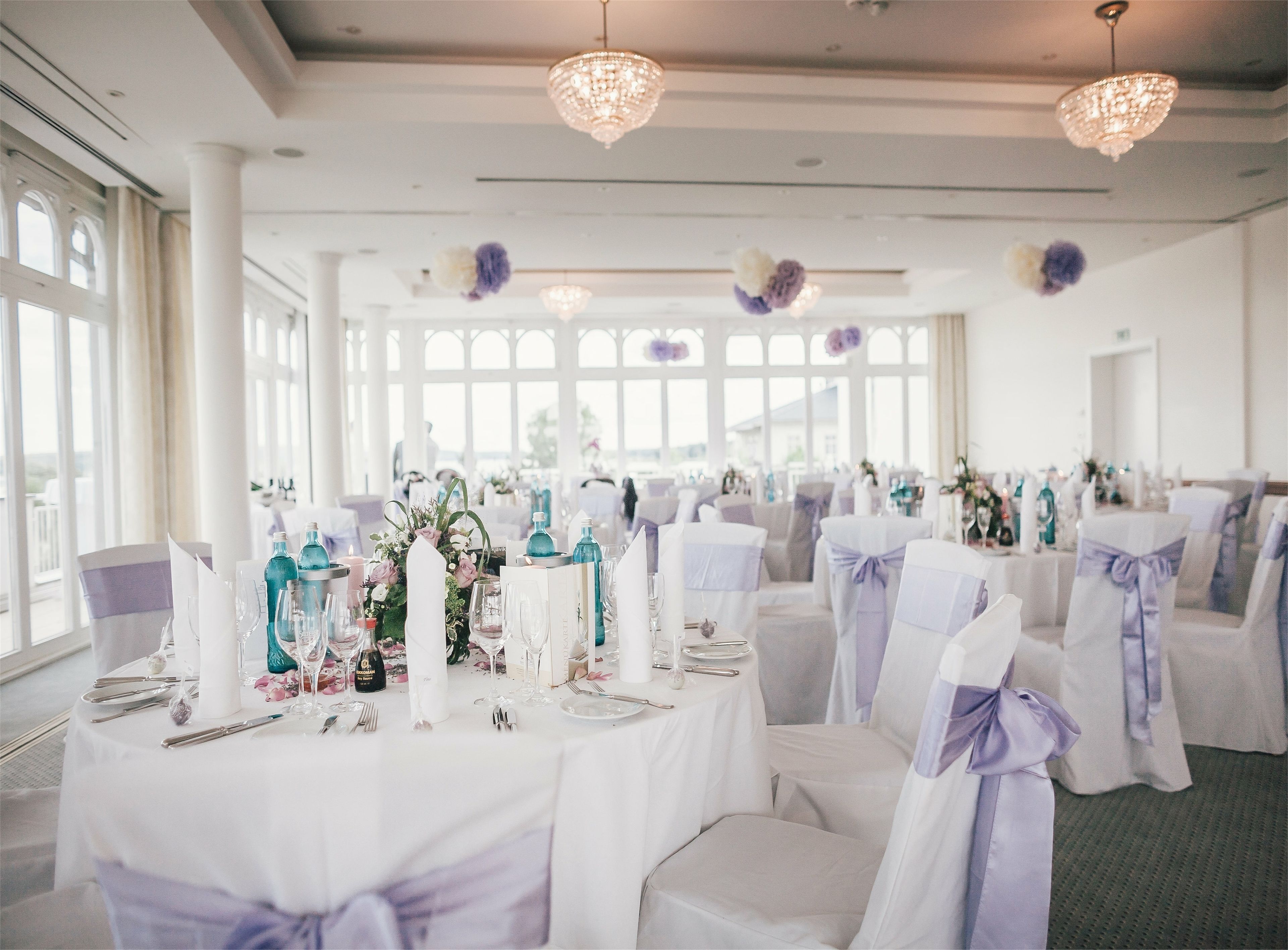 A banquet hall with round tables set for a formal event, featuring white tablecloths, glassware, and floral centerpieces.