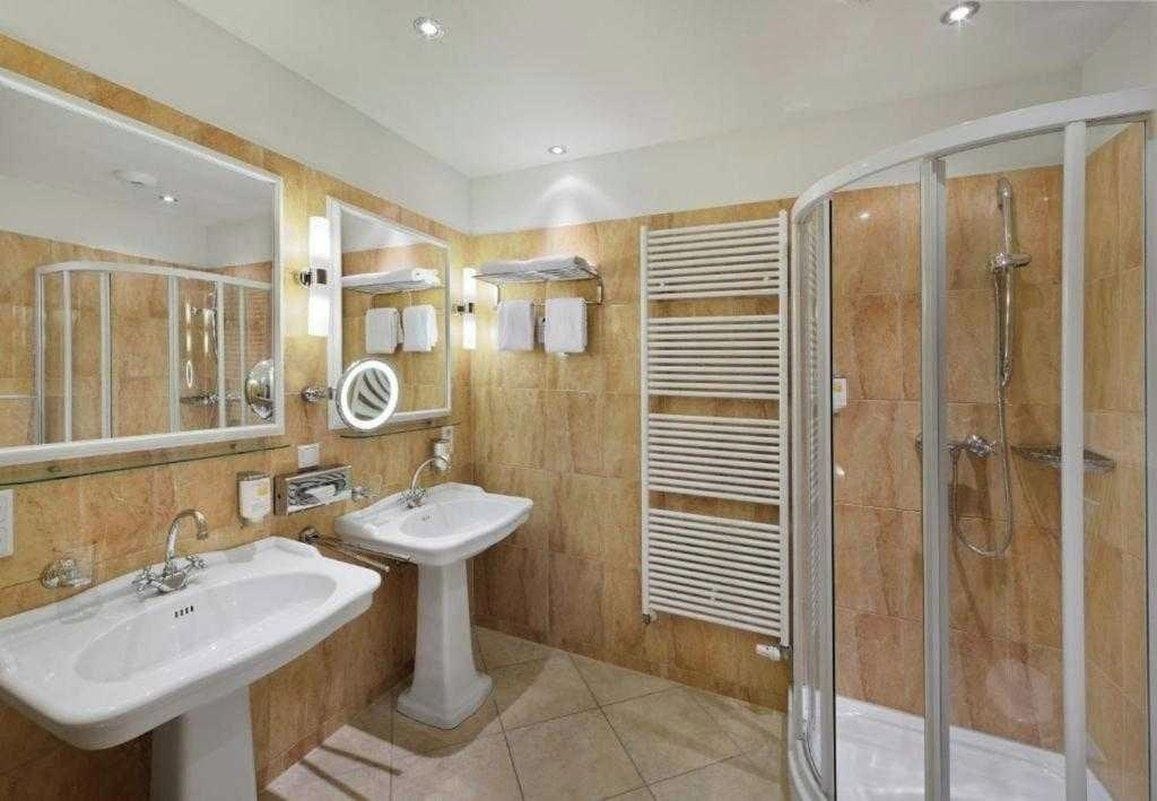 Un baño moderno con dos lavamanos, cabina de ducha con mampara de vidrio y un perchero para toallas.