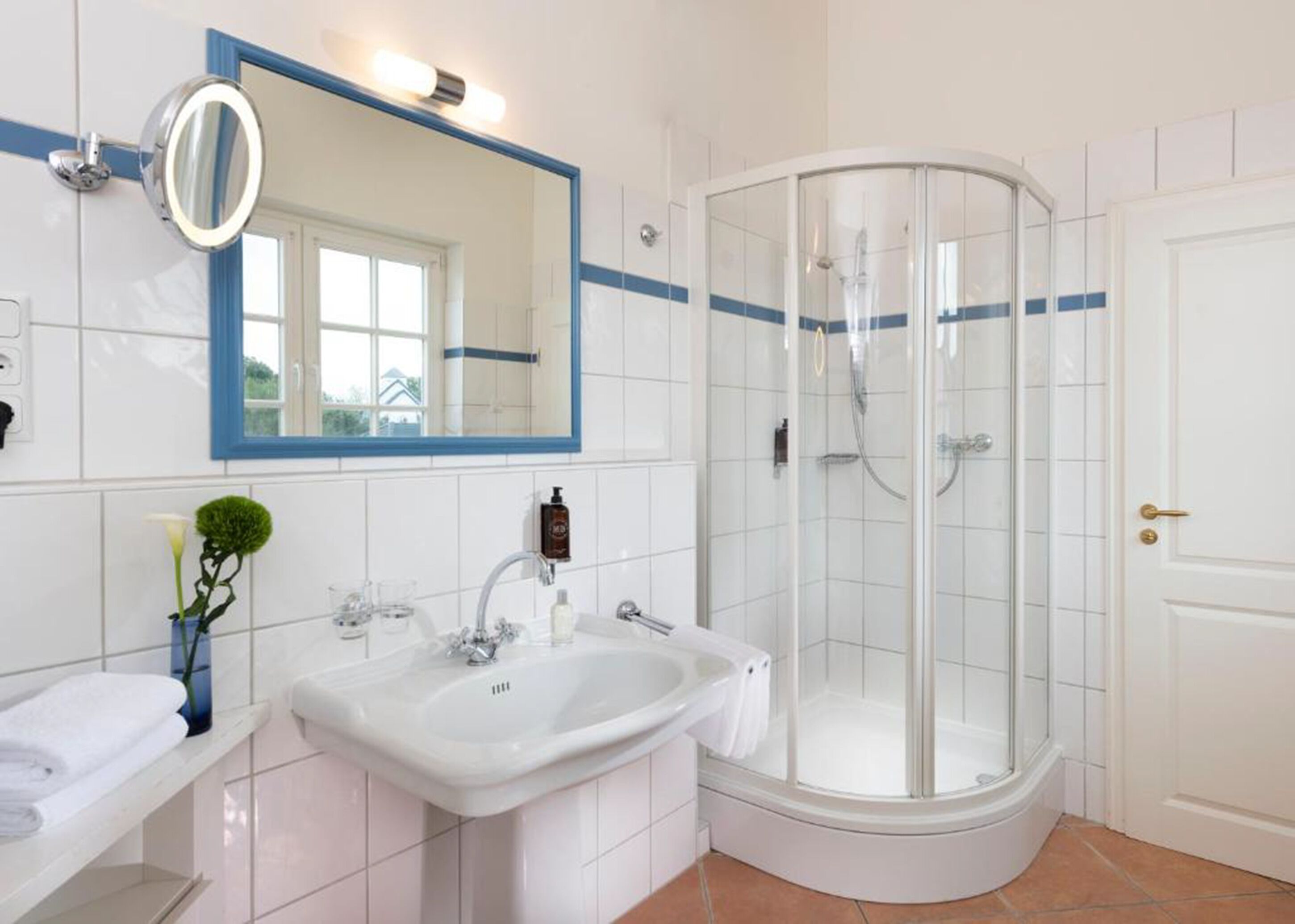 A modern bathroom with a white sink, a mirror, a glass-enclosed shower, and a door.