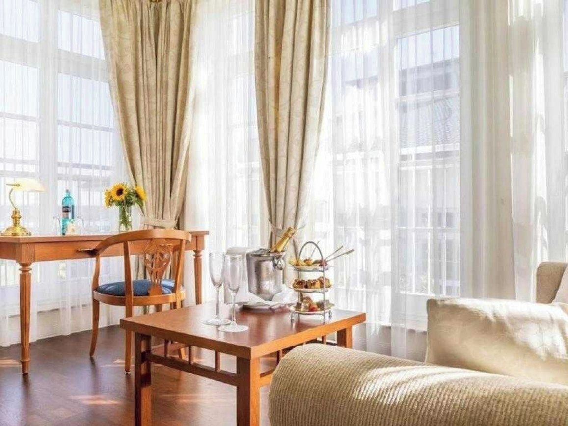 Una habitación con una mesa de comedor de madera, una silla, un sofá y una ventana con cortinas traslúcidas.