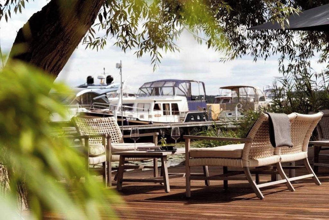 A wooden deck with wicker furniture and a view of boats in the background.