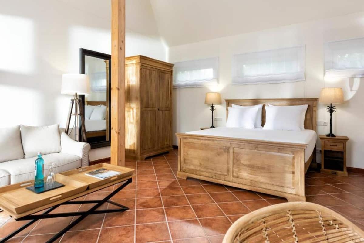 A bedroom with a large bed, a wooden wardrobe, a sofa, a coffee table, and two bedside lamps.