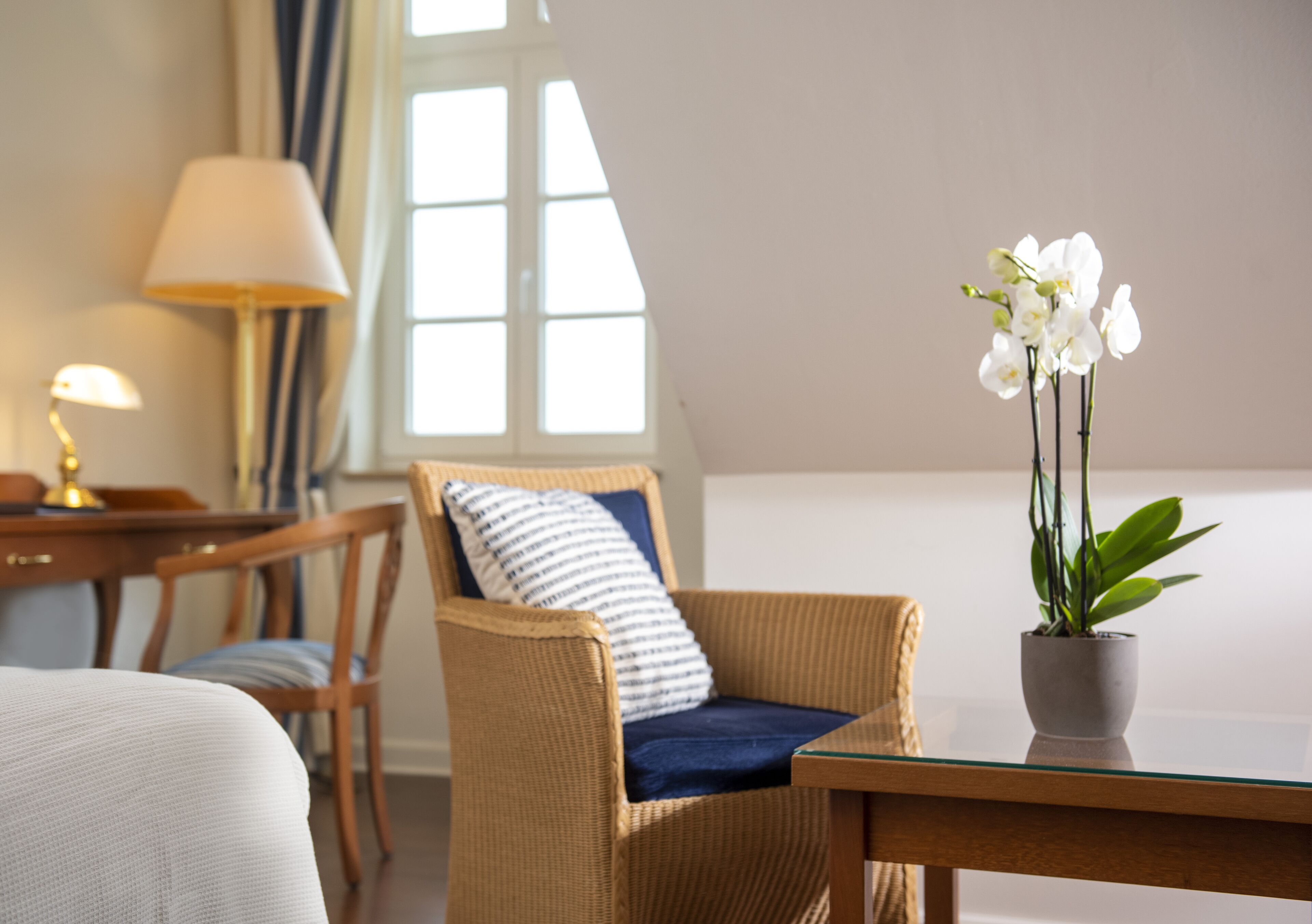 A room with a wicker chair, a small table with a potted orchid, and a lamp.