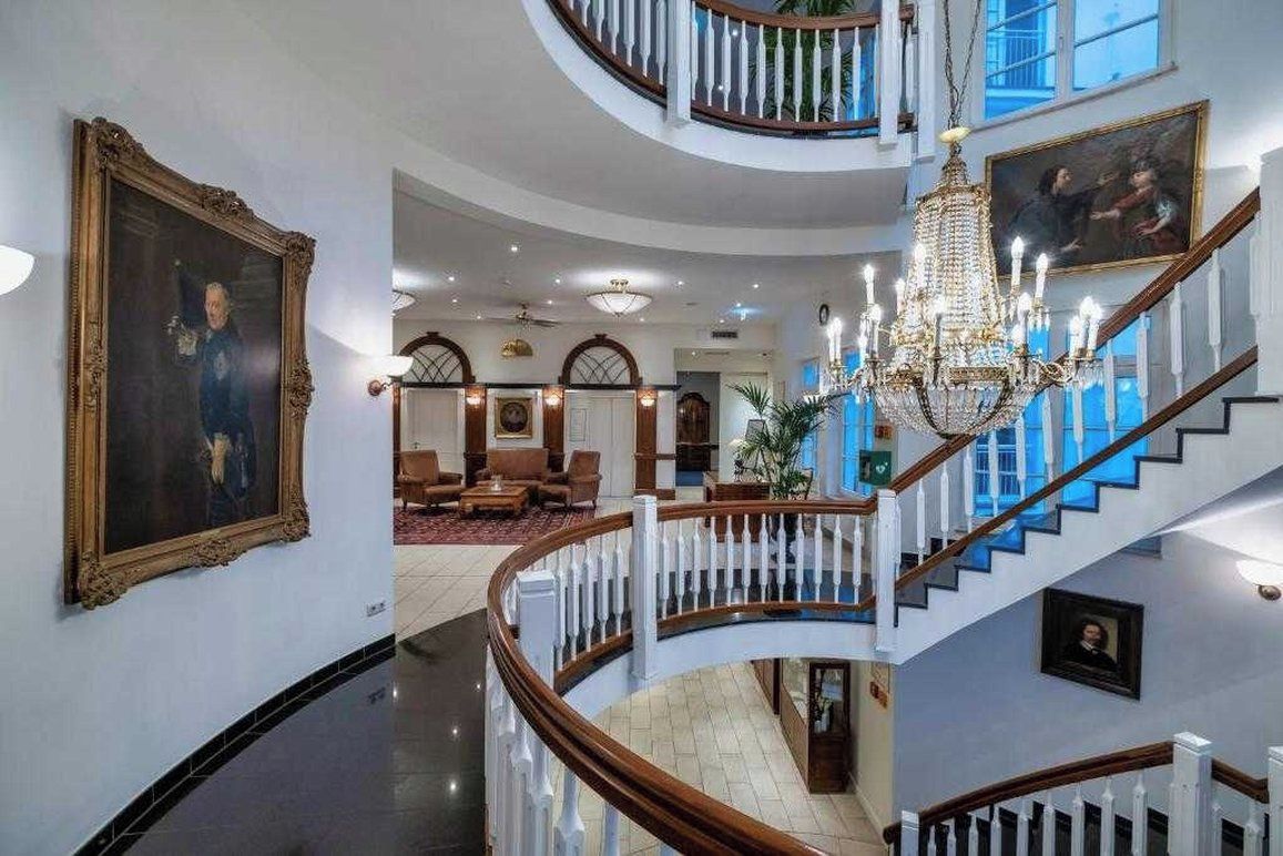 Ein prachtvolles Interieur mit einer zentralen Treppe, Kronleuchtern und gerahmten Kunstwerken an den Wänden.