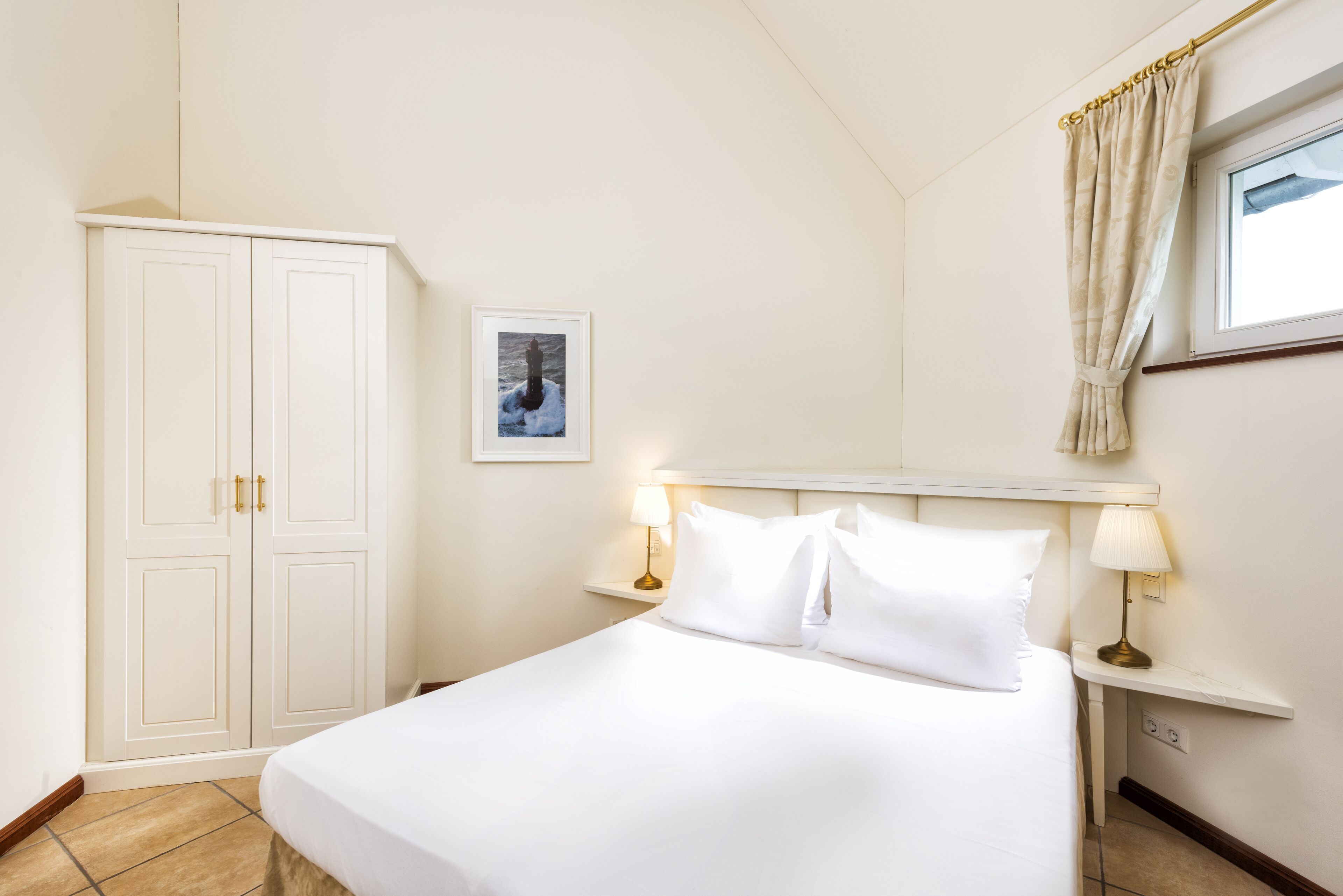 Ein Hotelzimmer mit einem großen Bett, zwei Nachttischen mit Lampen, einem Kleiderschrank und einem gerahmten Bild an der Wand.