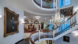 Un interior imponente con una escalera curva, candelabros y decoración clásica.